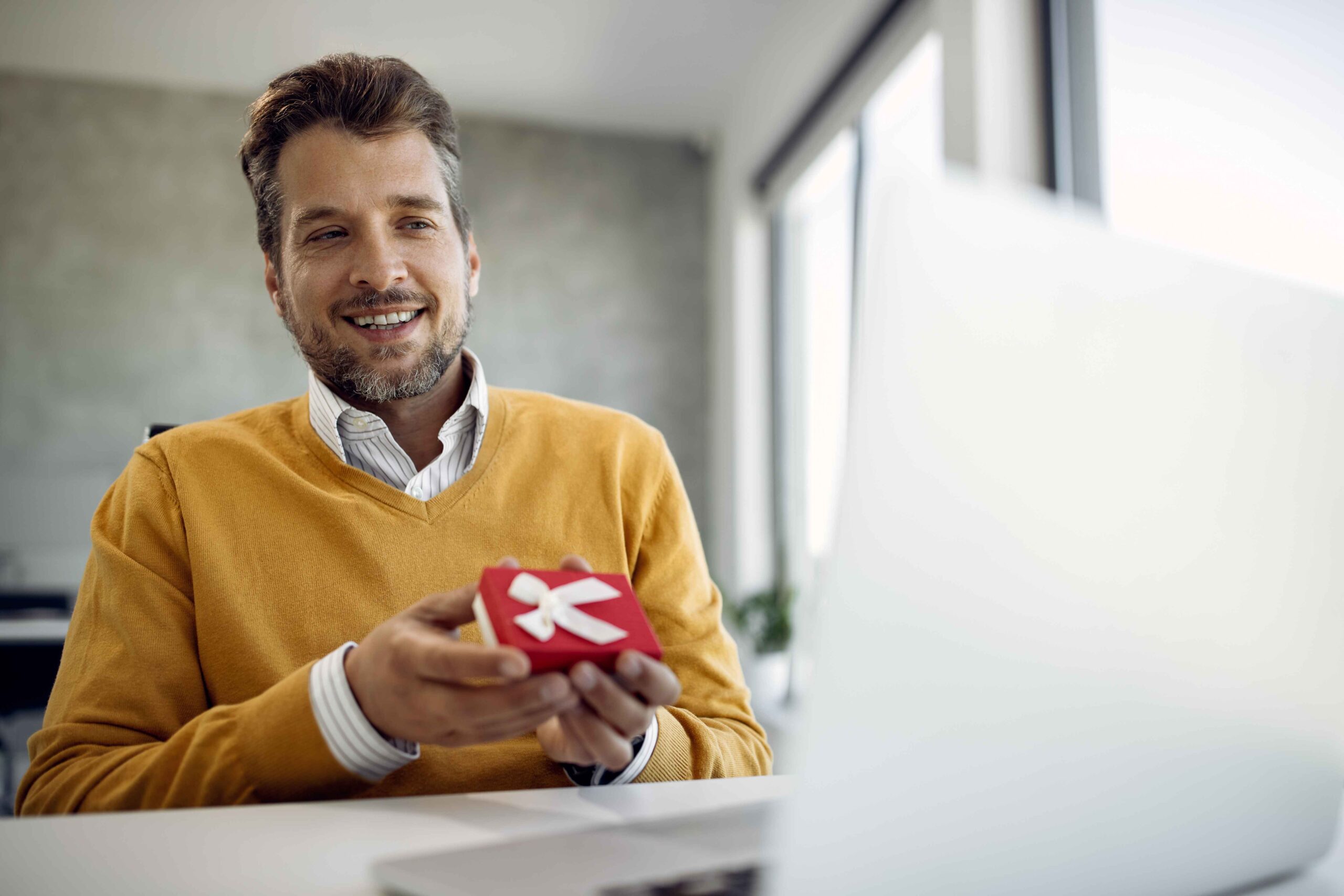 happy-businessman-holding-small-gift-box-while-making-video-call-laptop